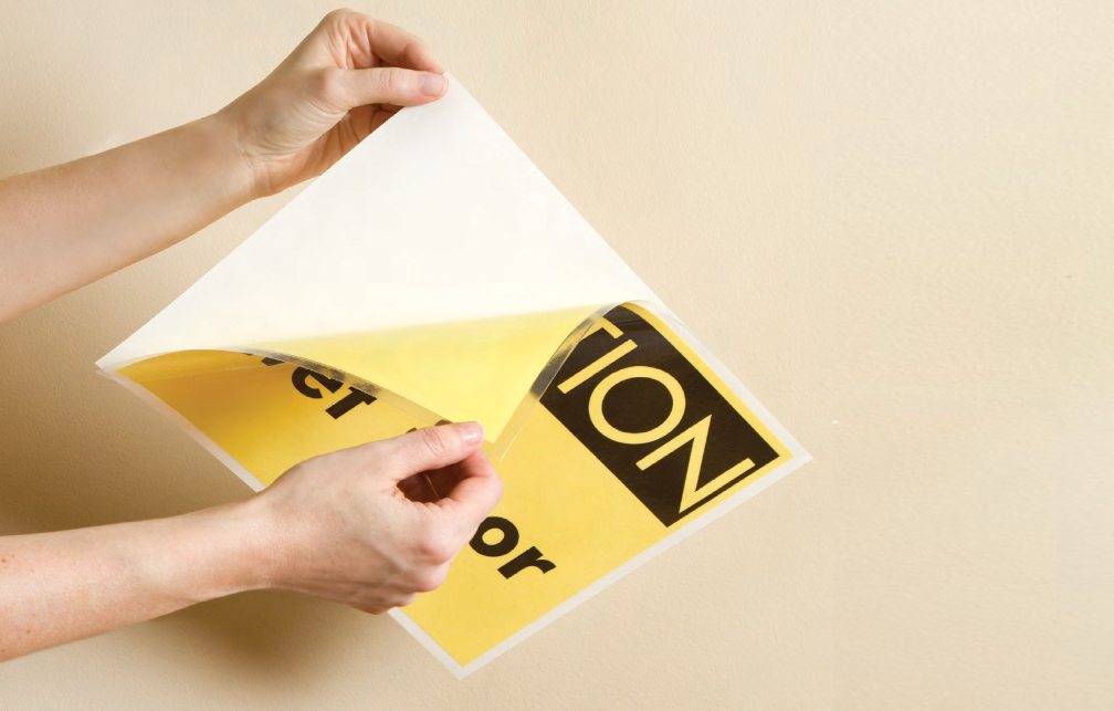 hands peeling laminated CAUTION SIGN